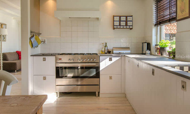 A photo showing a large clean kitchen with a dining table and two chairs on the left and two large windows on the right.