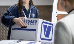 A photo showing a Vanguard employee carrying a Vanguard cardboard box for a customer.