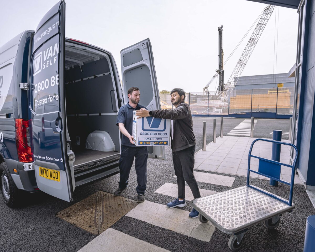 A photo showing a Vanguard employee helping a customer move boxes from a van and onto a trolley.