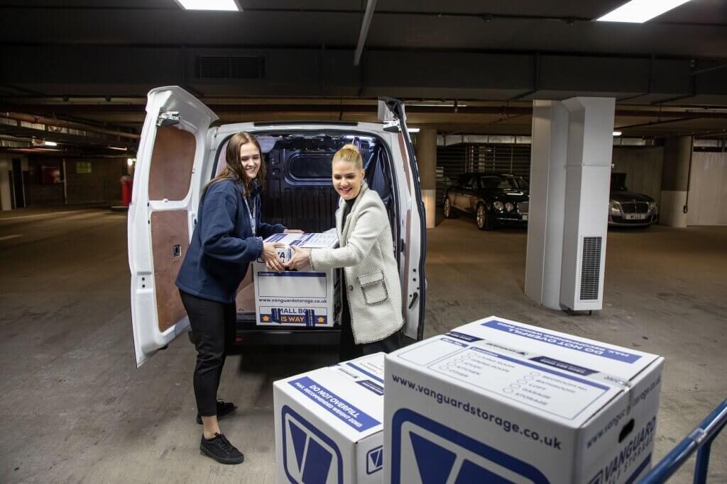 A photo of a Vanguard employee helping a customer move boxes from the car boot to the trolley.
