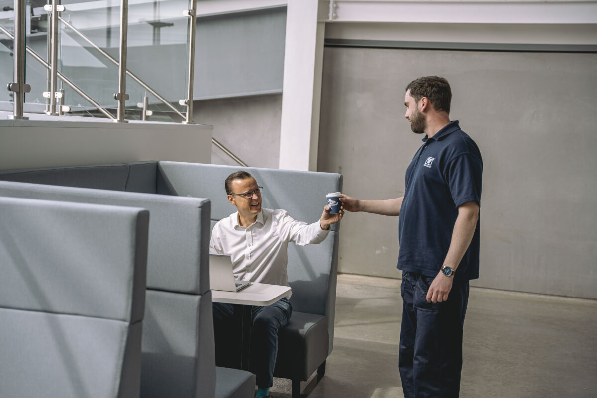 A photo showing a vanguard employee handing a man a coffee inside one of Vanguard Self Storage branches.