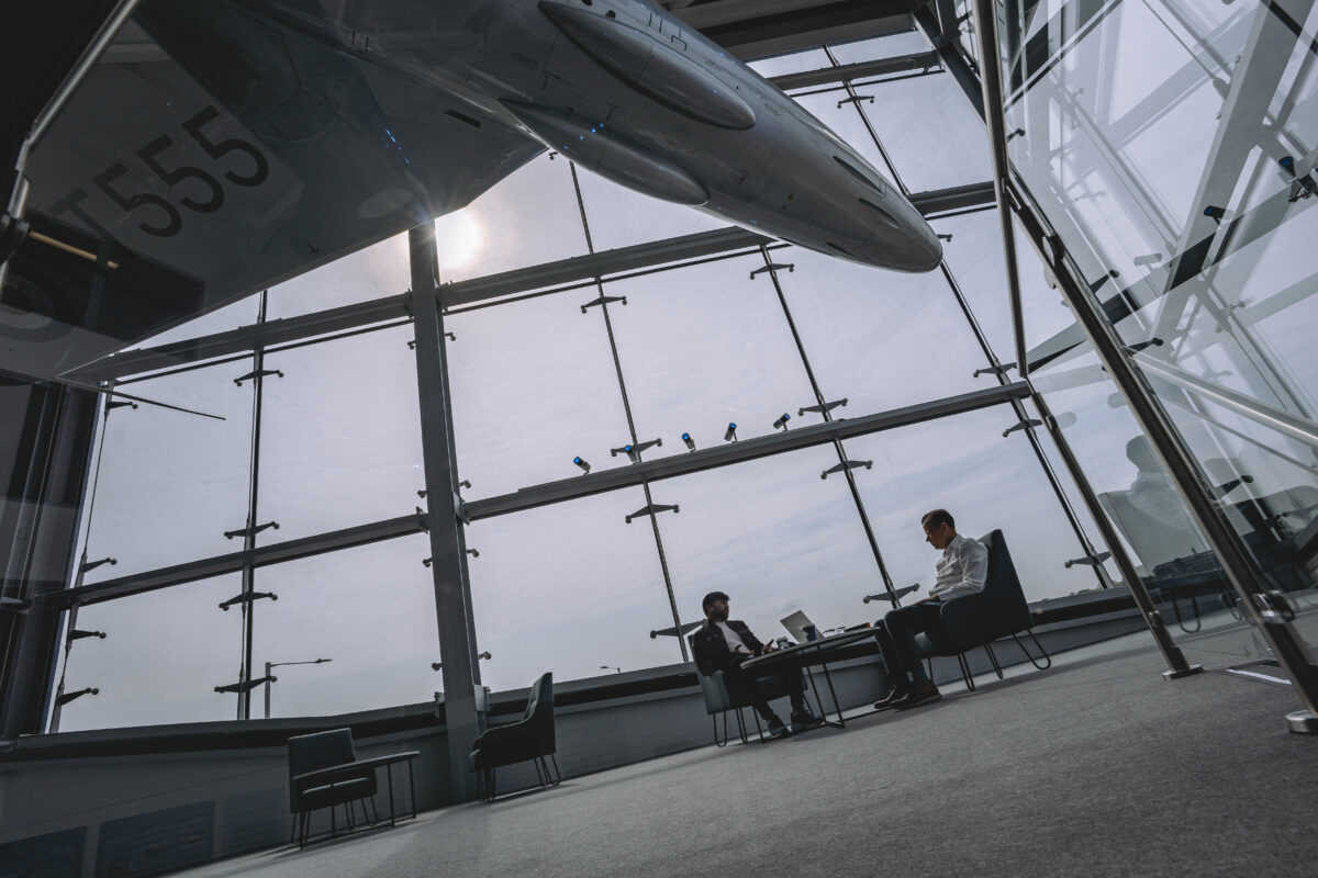 A photo showing the interior of Vanguard Self Storage branch in Staples Corner. The photo shows two men chatting sitting at a table and the English Hawker Hunter F1 fighter jet plane hanging in the reception.