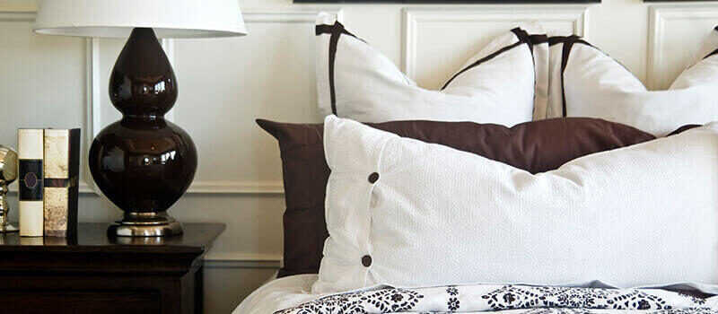 A photo showing a bed next to a bedside table with some books and a lamp on it.