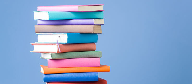 A photo showing a stack of colourful books against a blue background.