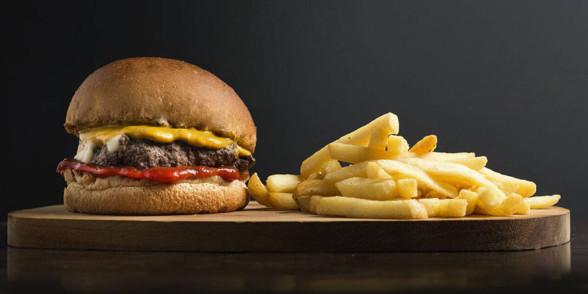 A photo showing a cheeseburger and fries on a round wooden serving board.