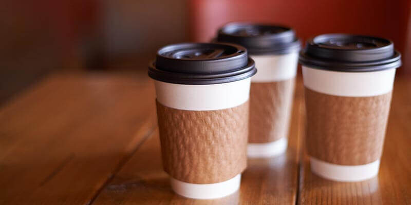 A photo showing three paper coffee cups on a wooden table.