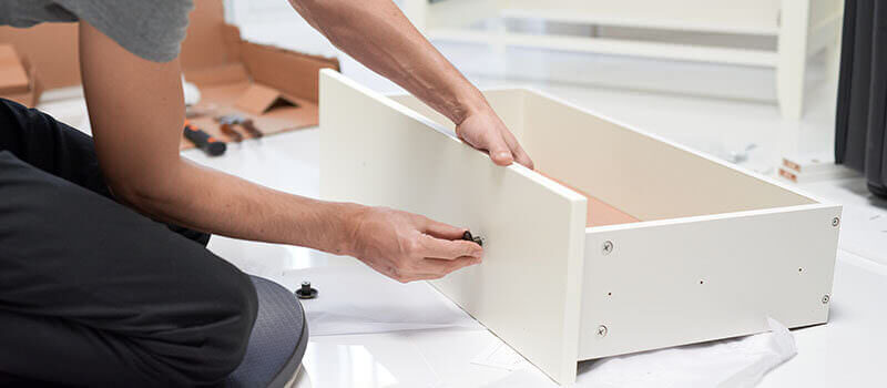 A photo showing a person installing furniture and adding handles to a drawer.