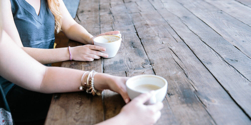 A photo showing two women holding mugs and drinking coffee together.