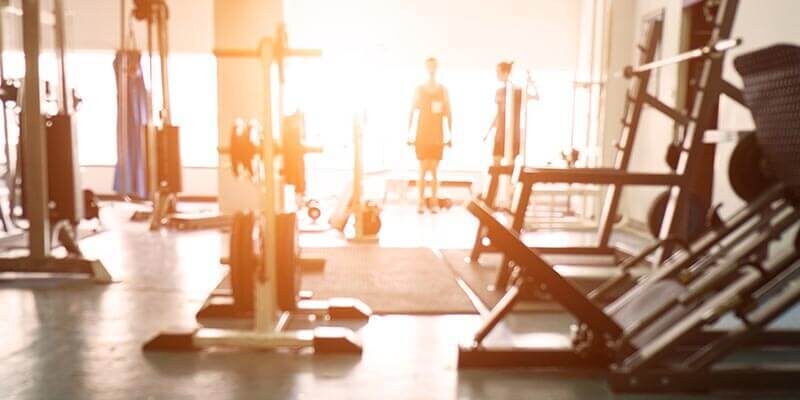 A photo showing the inside of a gym with two people working out in the background.
