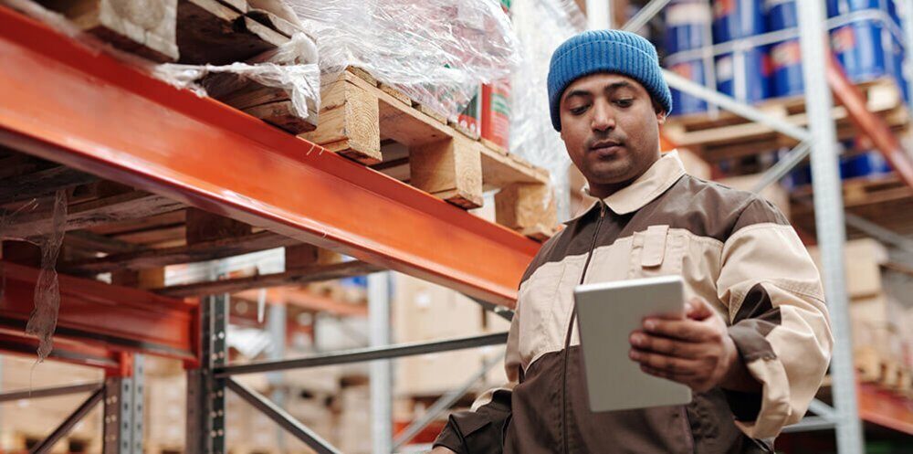 A photo showing a man holding a notebook inside of a warehouse, managing inventory.