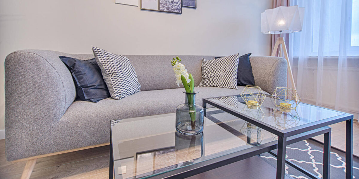 A photo showing a sofa in front of a glass coffee table and next to a tall lamp in a living room.
