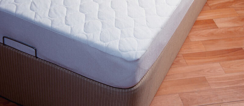 A photo of a close-up of a mattress with a wooden floor in the background.