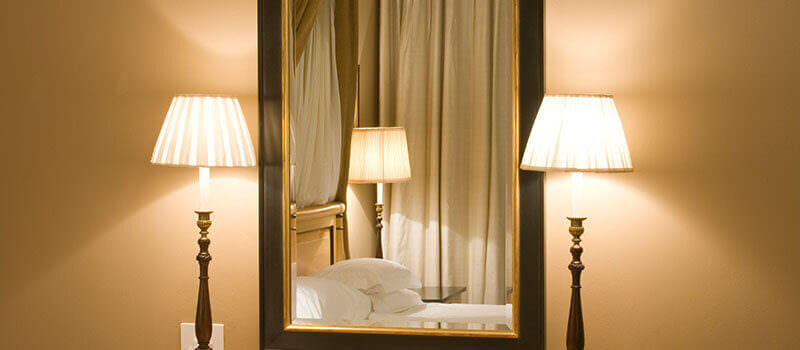 A photo of a mirror showing the reflection of a bed between two lamps.