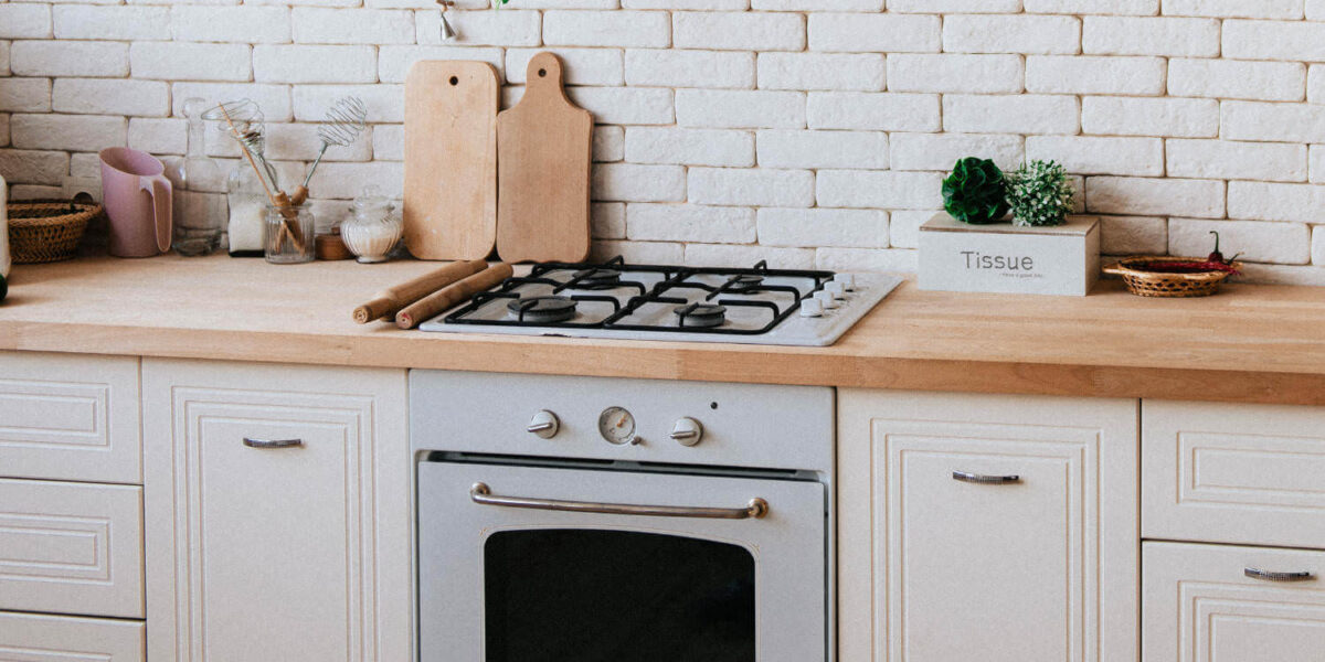 A photo of a kitchen with wooden chopping boards, utensils and ornaments against a white brick wall.