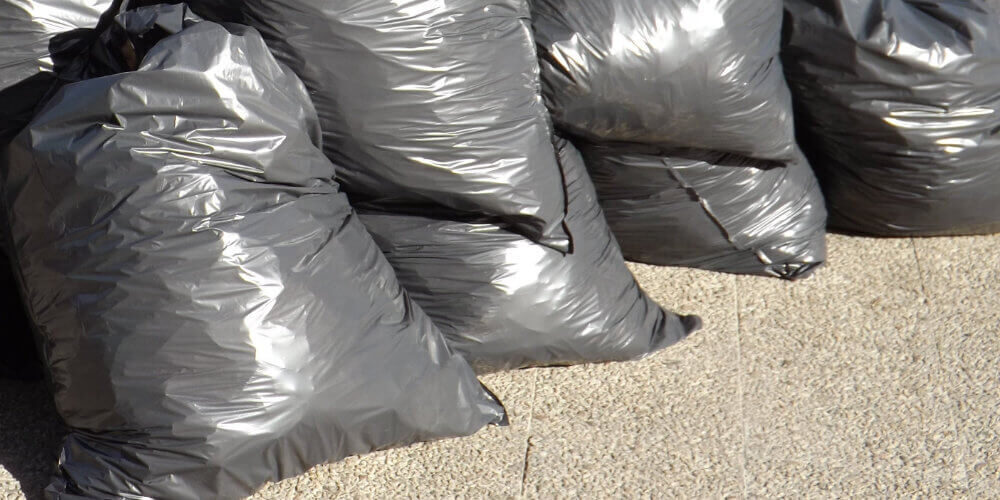 A photo showing several full black rubbish bags on the floor.