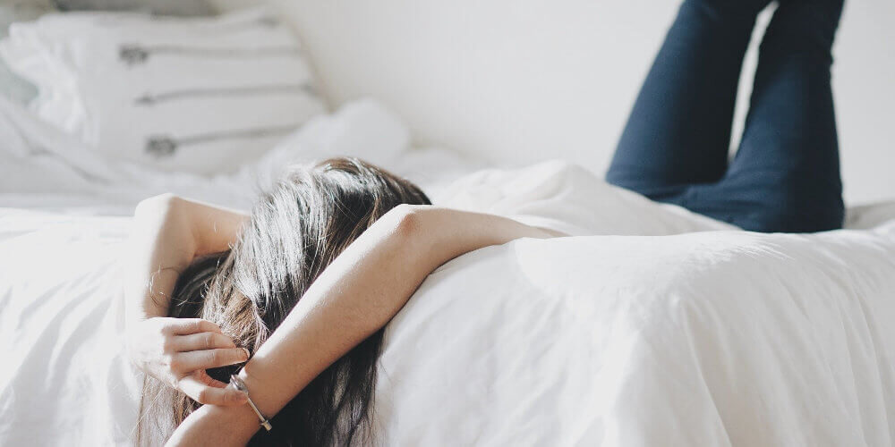 A photo of a woman laying on a bed with her legs up resting against the wall.
