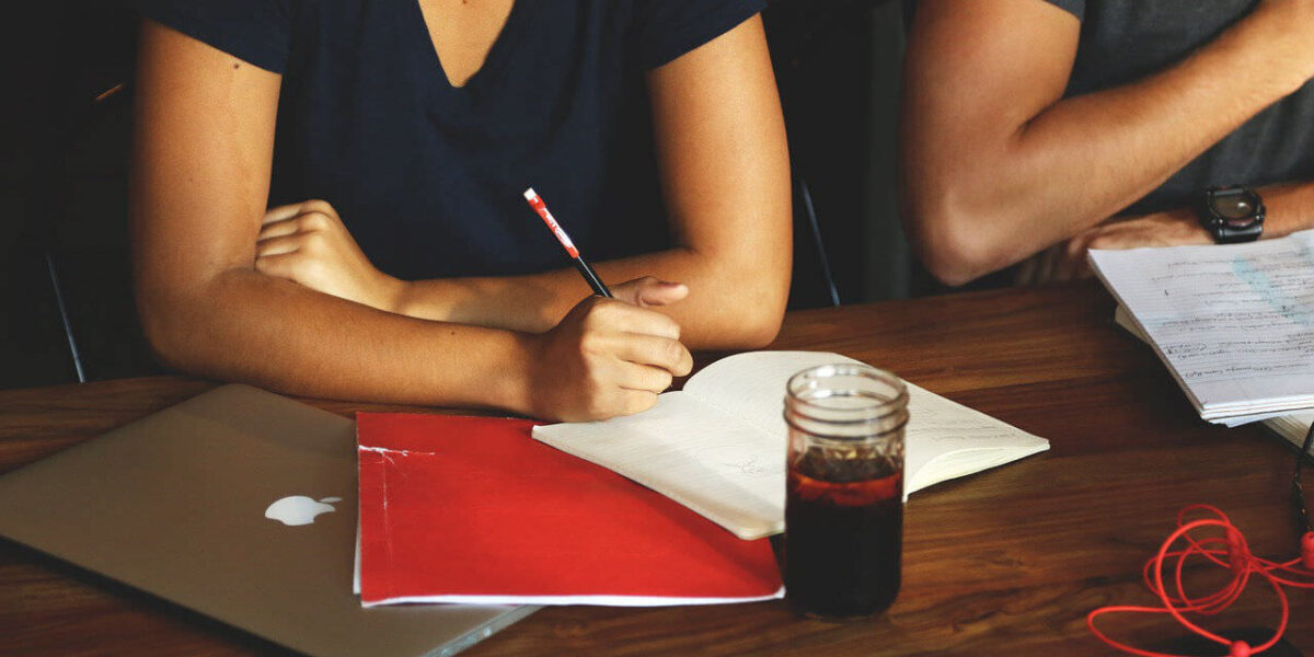 A photo of two people with pens and notebooks and a soda in a glass in front of them.