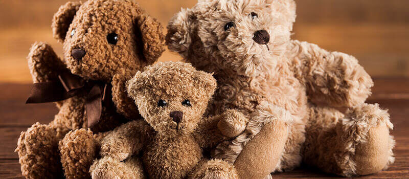 A photo showing three stuffed bear toys on a wooden table.