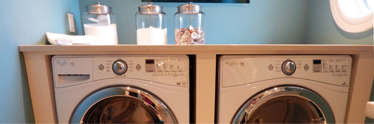 A photo of a utility room with a washing machine and tumble-drier and three detergent containers on top.