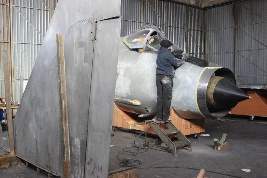 A photo showing the restoration process of the fighter jet hanging in the Vanguard Staples Corner branch.