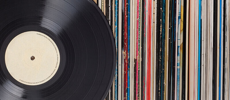 A photo showing a large collection of vinyls in their sleeves, with a black vinyl on top.