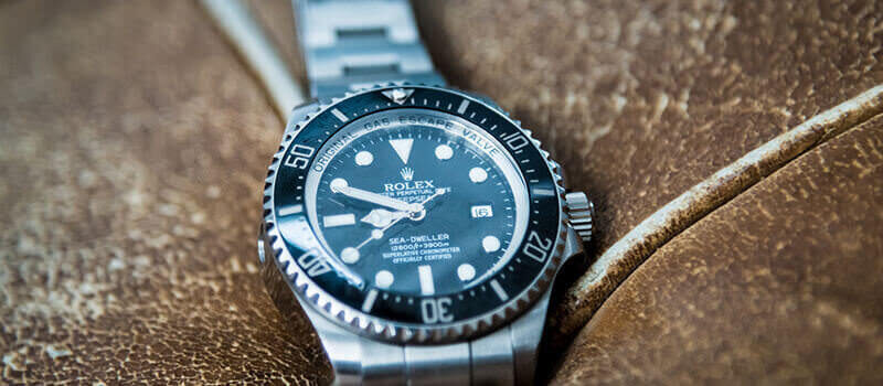 A photo showing a close up on a silver Rolex watch on a brown suede background.