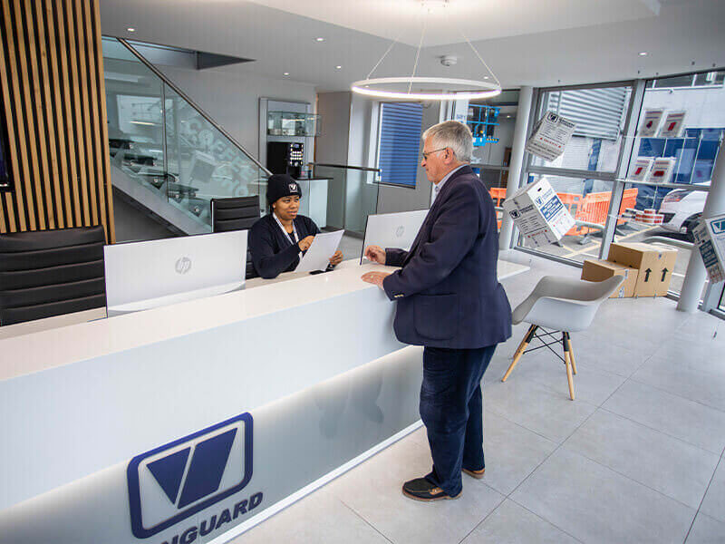A photo showing a Vanguard employee working at the reception at the West London branch and greeting a customer.