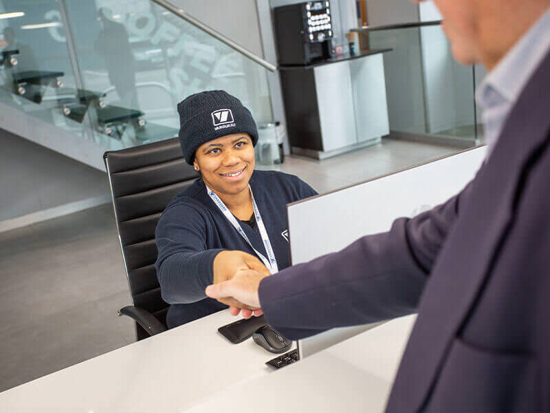 A photo showing a Vanguard employee working at the reception at the West London branch and greeting a customer.