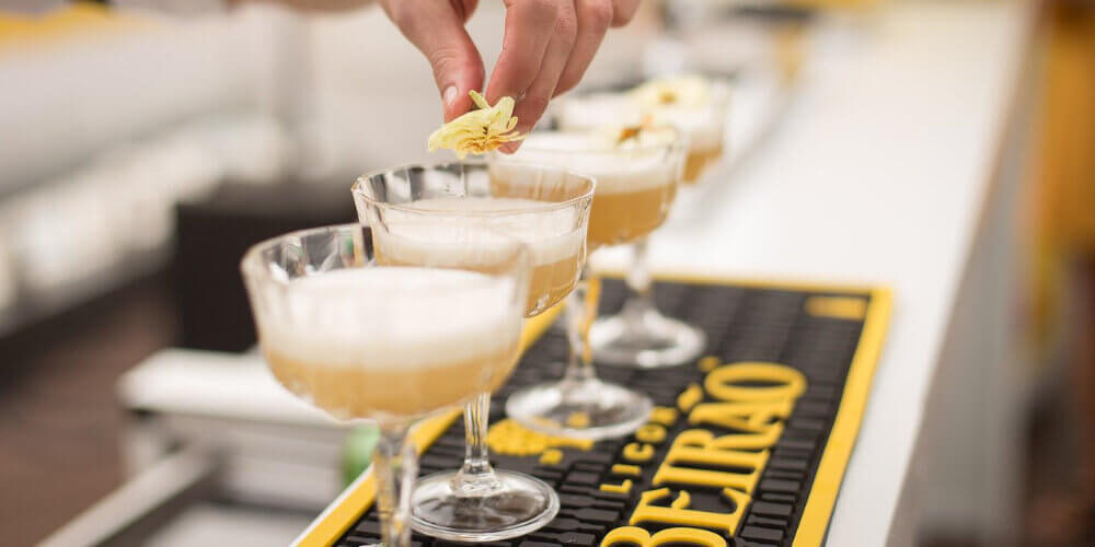 A photo showing a bartender in front of four cocktails and adding garnish to one.