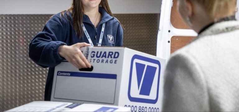 A photo showing a Vanguard employee carrying a Vanguard cardboard box for a customer.