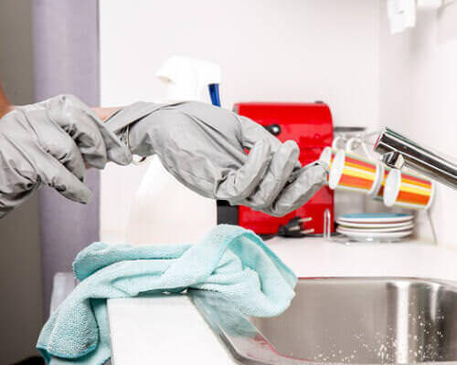 A photo of a person removing rubber gloves in the kitchen sink.