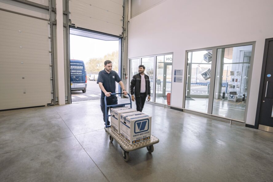 A photo showing a Vanguard employee pushing a trolley with Vanguard cardboard boxes on it for a customer.