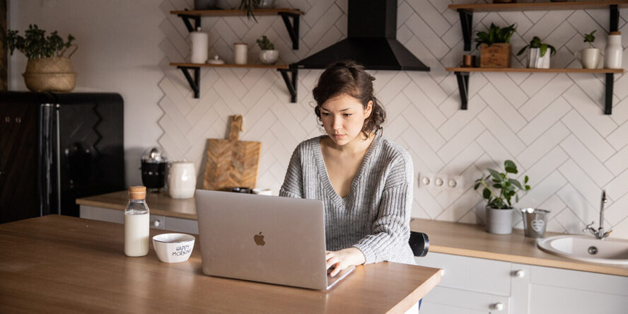 A photo showing a woman in front of a laptop in a kitchen.