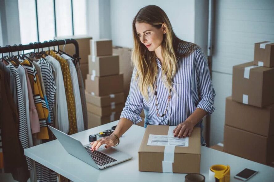 A photo showing a woman in front of a laptop while packing a parcel inside of a storage unit.