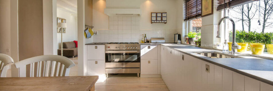 A photo showing a large clean kitchen with a dining table and two chairs on the left and two large windows on the right.